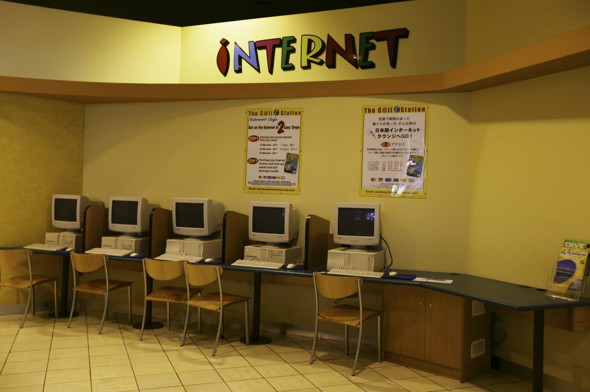 A row of computers on a bench-desk. There is a big colourful sign saying INTERNET above them.
