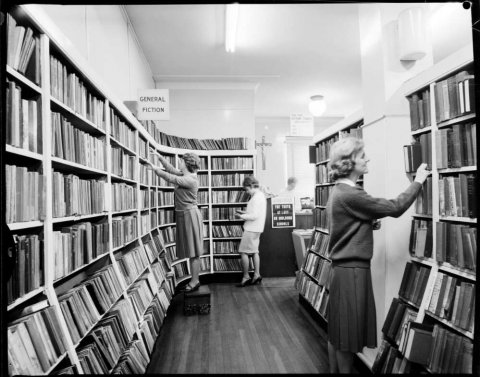 Three women looking at books in front of bookshelves