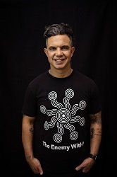 A portrait image of a smiling man wearing a black t-shirt with a white artwork printed on it.