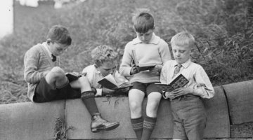 Four young boys reading books on top of a stone wall at school, New South Wales, ca. 1930 