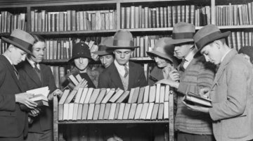 Nine people gathered around trolley of books in a library