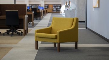 A modern yellow armchair in the centre of a large carpeted room