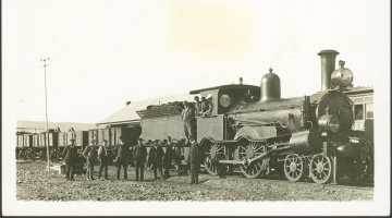 A sepia toned photograph of a group of men standing in front of a steam engine train