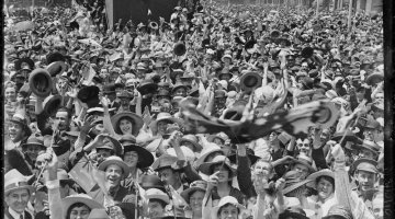 Black and white photograph of a crowd of people in the streets cheering, laughing and celebrating
