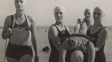 Four women lifesavers carrying a fifth woman in from the beach