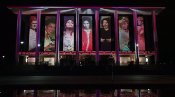 Exterior of the National Library building illuminated at night, featuring images of female performers