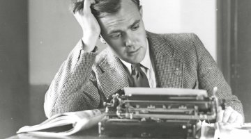 A man in a suit sits at a typewriter