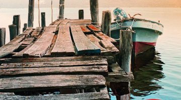 An image of an old, rickety jetty on the water, with a small boat ties up to it.