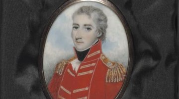 A painted locket portrait of a man in a red military uniform. The locket is resting on some black material.