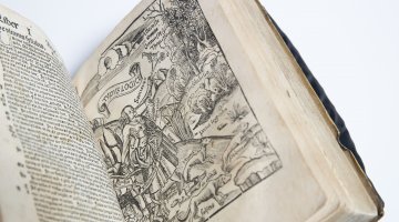 A rare book opened to a page of text on the left and detailed illustration of a person, some animals and nature. 