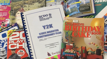 Magazines and books from the 00s and 90s spread out, including the 'Australian Women's Weekly: Children's birthday cake book' and a document titled 'Y2K: State disaster contingency plan'
