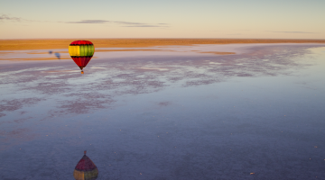 Hot air balloon flying over a huge lake and desert area that stretches out towards the horizon at dawn 