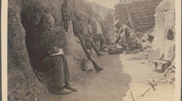 Sepia toned photo of soldiers sitting in a trench writing letters
