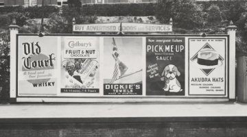 Advertising billboard for Old Court whisky, Cadbury's chocolate, Dickie's towels, Pick-me-up Worcestershire sauce and Akubra hats on railway platform, Melbourne, ca. 1930