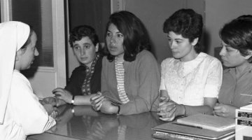Social worker Sister Margherita speaking to four young South American migrant women over a counter at the Catholic Family Welfare Bureau in Sydney