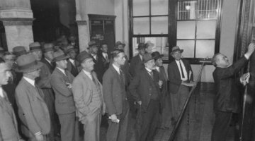 Crowd of men watching a man write on a blackboard at the Sydney Stock Exchange