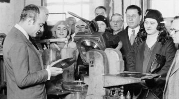 Mischa Levitzki and crowd of people standing around a vinyl record machine inspecting a vinyl record