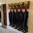 A row of firefighter uniforms with hats and boots are hung in a row on display