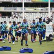 Young men of the Fijian Drua rugby union team wearing green and blue uniforms walking or jogging on rugby field near goal post