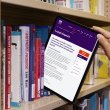Tablet being pulled from a bookshelf like it's a book. On the screen is a page from the National Library's website sharing information about 'Legal Deposit'