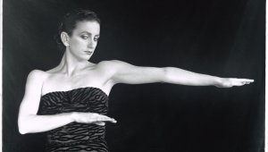 Ballerina Meryl Tankard strikes a pose. She is wearing a zebra print-esque dress. She is standing in front of a black curtain.