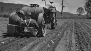 A black and white photograph of two men driving a tractor through a field
