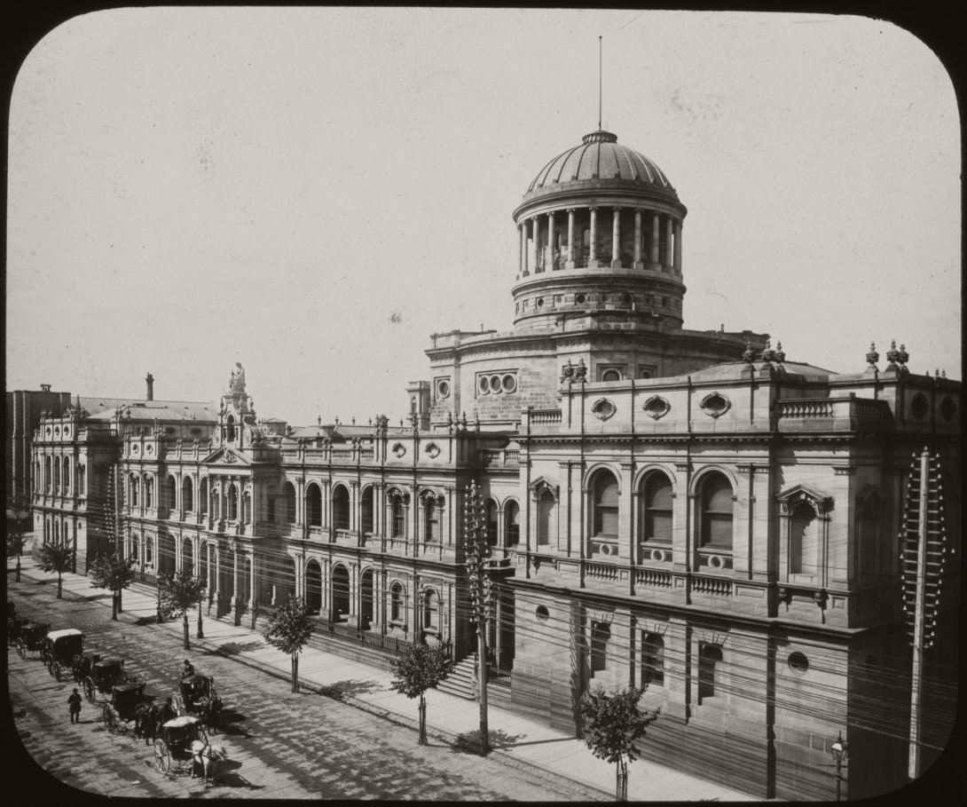 Black and grey slide with a large colonial era stone building with a dome in the centre stretching the full width of image. Road in front of the building is lined with trees