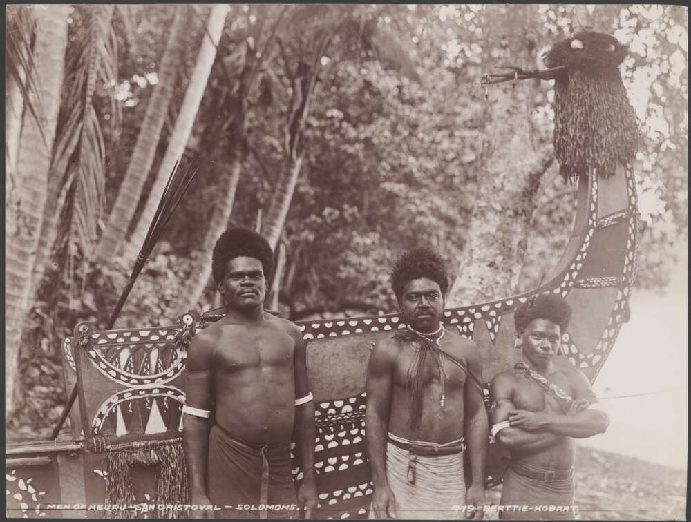 Three men standing in front of a painted canoe, Solomon Islands, 1906