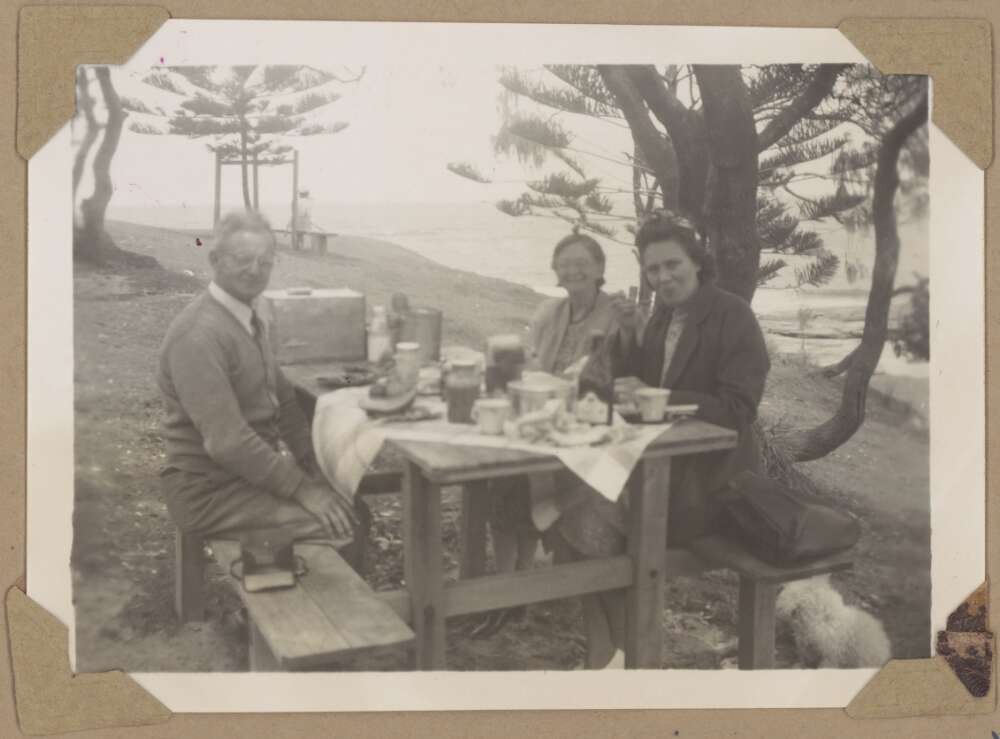 A group at an outdoor picnic table spread with tablecloth, food and drink