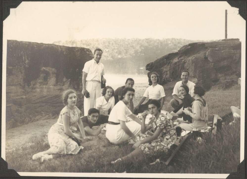 A group of people sitting outdoors with cliffs and ocean in the background
