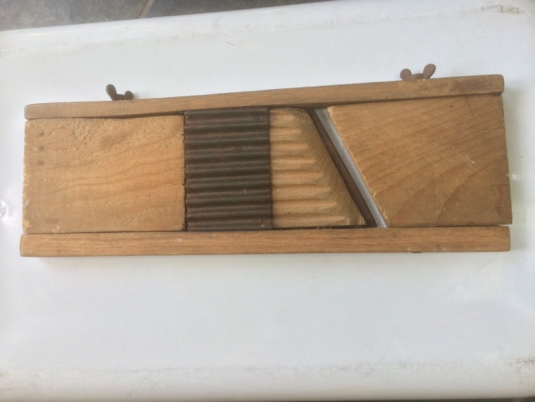 A wooden and metal mandolin slicer laid out on a white surface