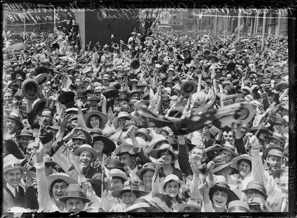 Black and white photograph of a crowd of people in the streets cheering, laughing and celebrating