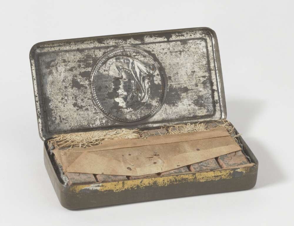 A small tin is open to reveal chocolates inside, partially obscured by paper. Both the tin and contents are very old.