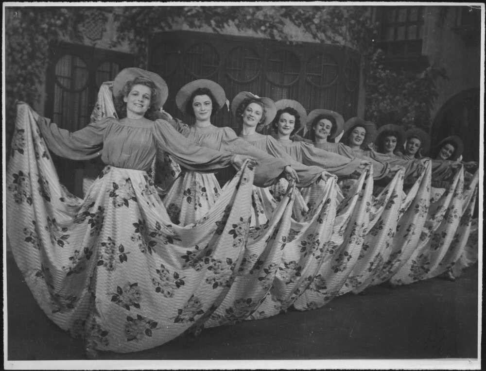 Black and white photograph of a row of women posed in matching costumes