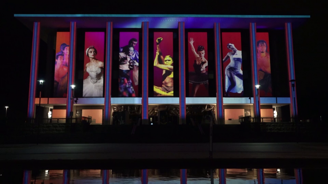 Exterior of the National Library building at light, illuminated with projections featuring dancers