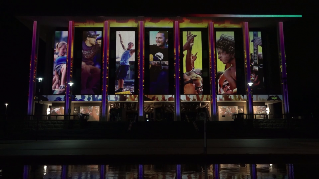 Exterior of the National Library building at light, illuminated with projections featuring live music performers