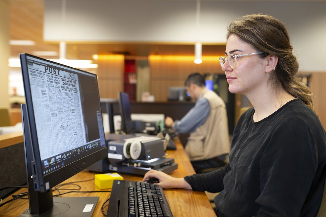 A woman in glasses uses a computer at a desk