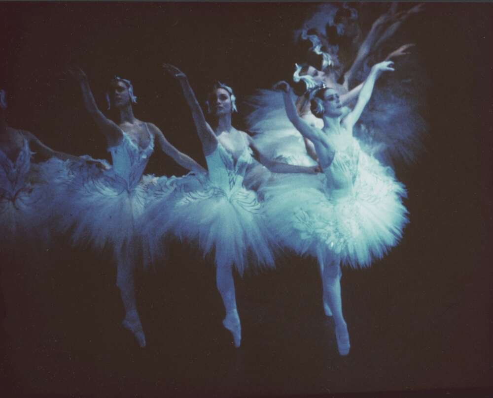 Three ballerinas mid-movement in matching white tutus
