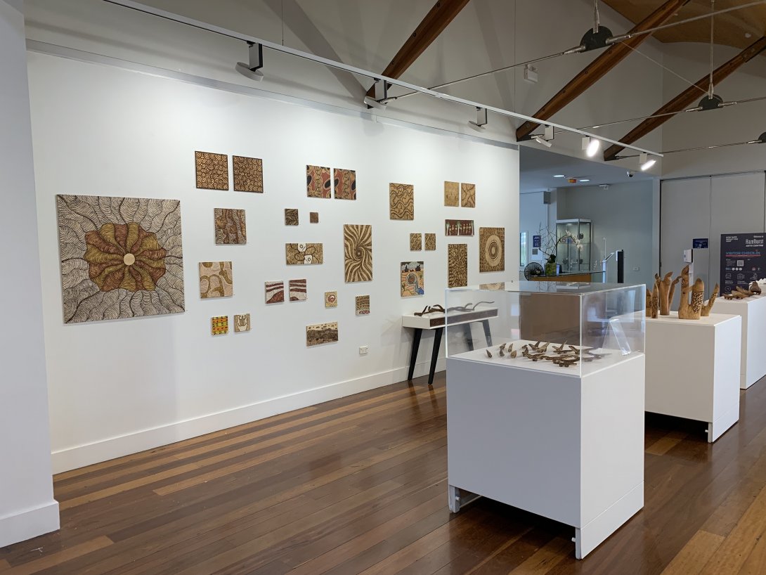Installation view of a gallery. Small 2D works are installed on the walls and objects displayed on white plinths.
