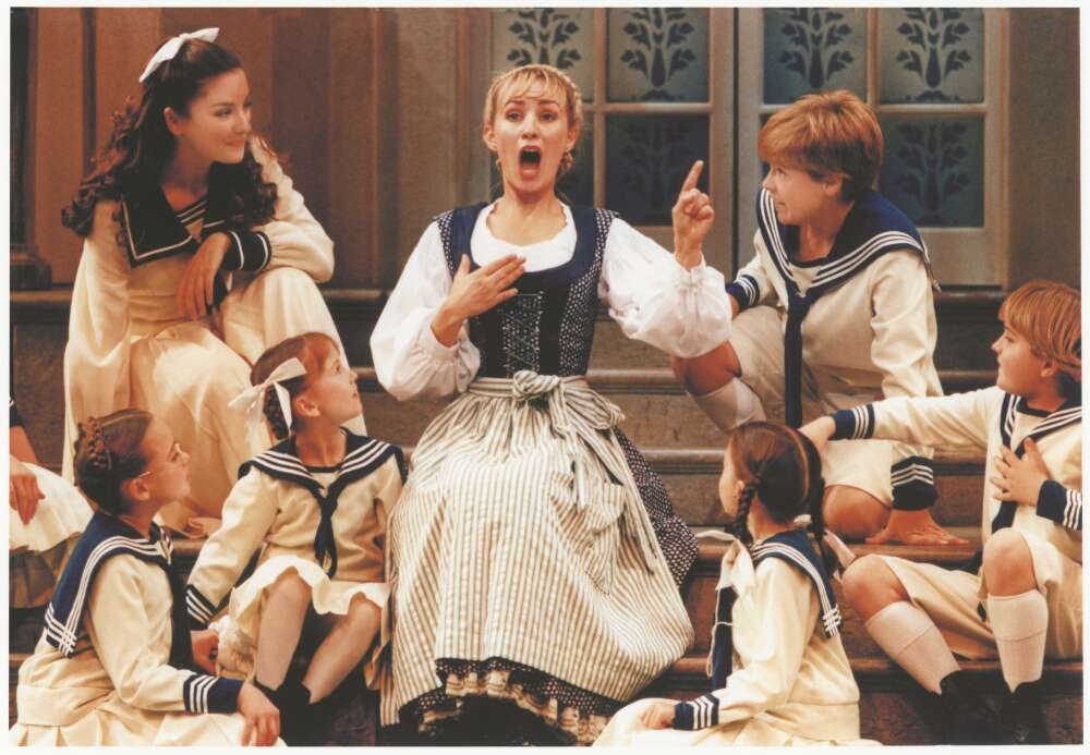 A woman sings while children in sailor suits gather around her