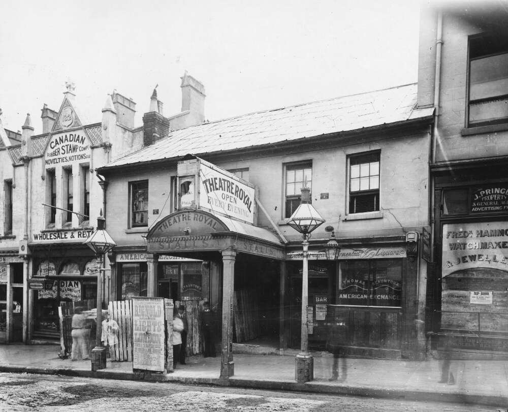 Black and white photograph of a row of shopfronts; one reads "Theatre Royal open"