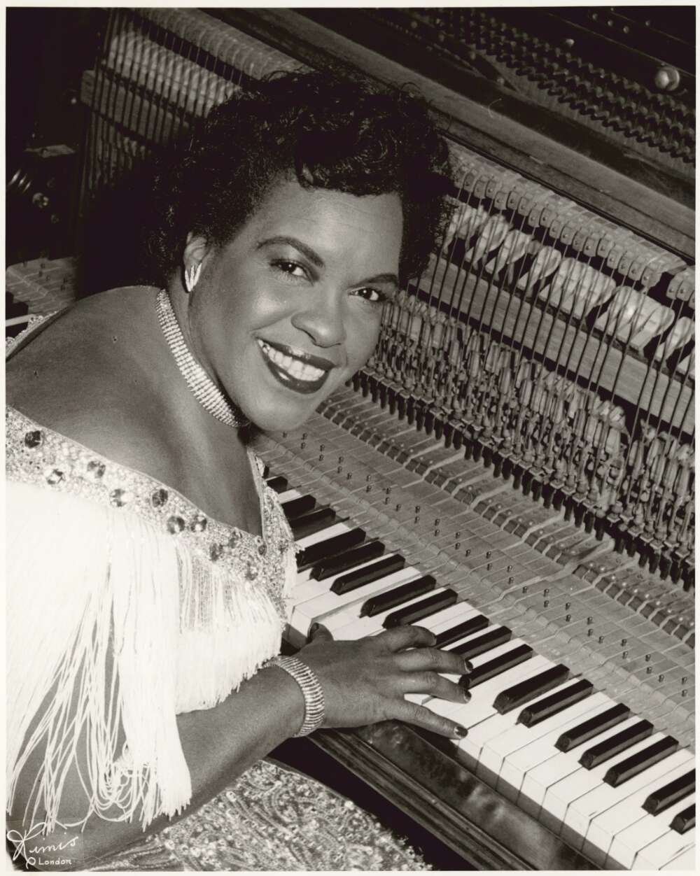 A woman sits at a piano with her head turned toward the camera, smiling