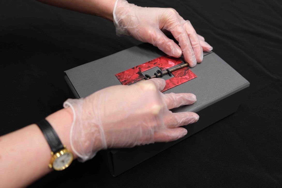 A black box with red detailing is being closed by a pair of gloved hands