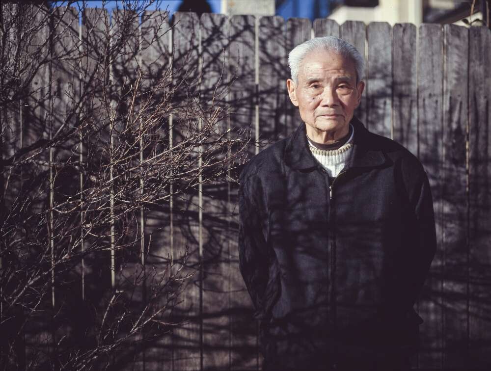 A man stands outside a tall wooden fence in daylight