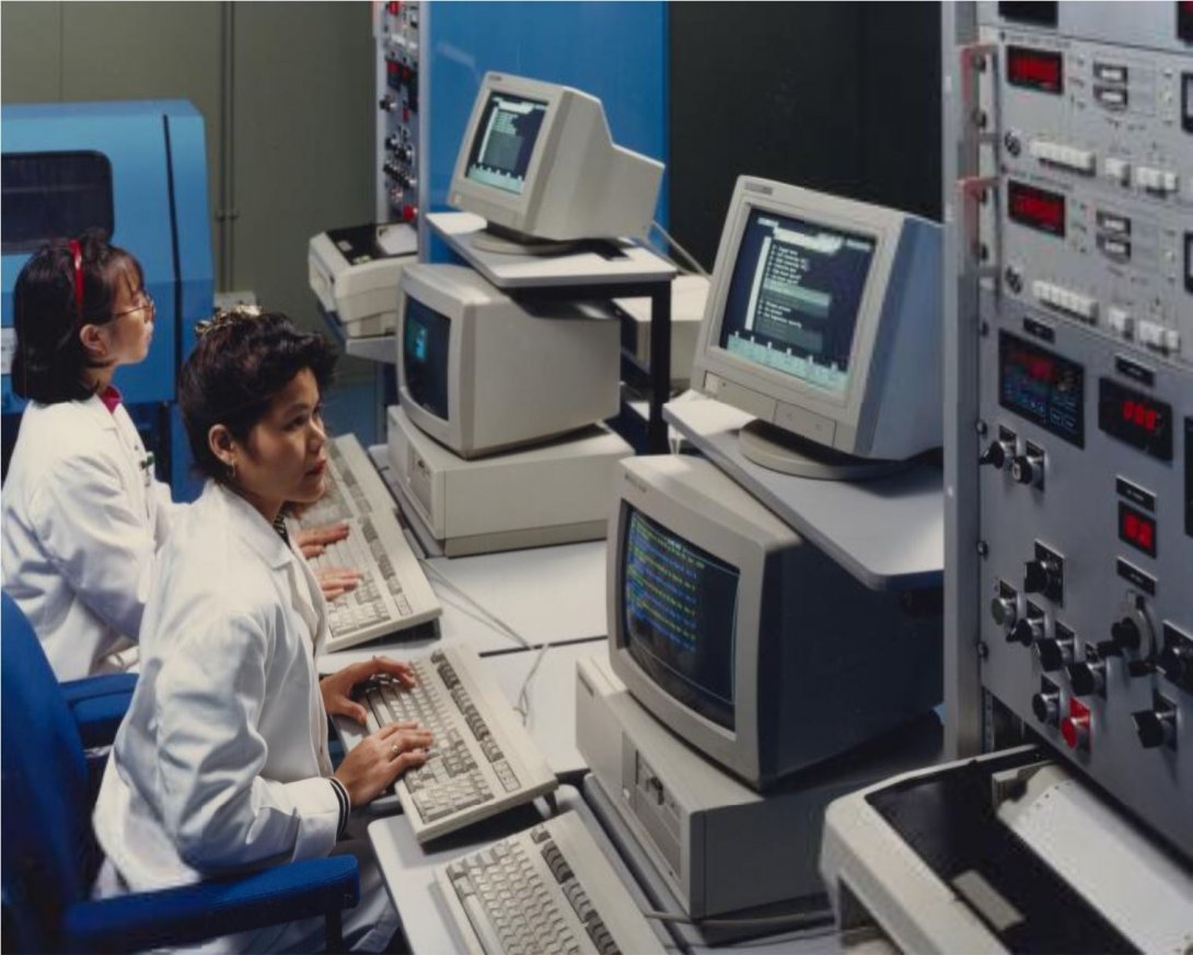 Two women in lab coats look at data on a computer screen