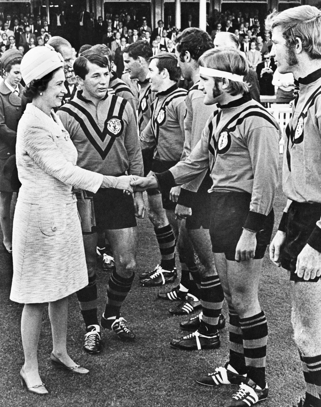 A black and white image of the Queen meeting and shaking hands with a team of rugby players.
