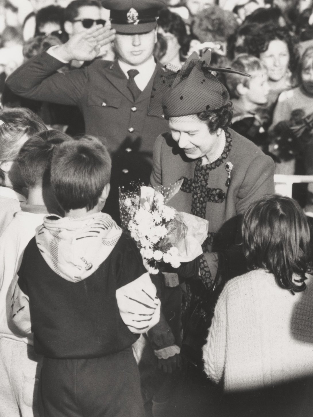 A black and white image of the Queen receiving a bouquet of flowers from a child.