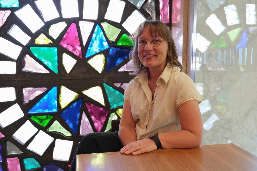 2022 Summer Scholar Deborah Lee-Talbot sitting in front of a stained glass window at the Library. 