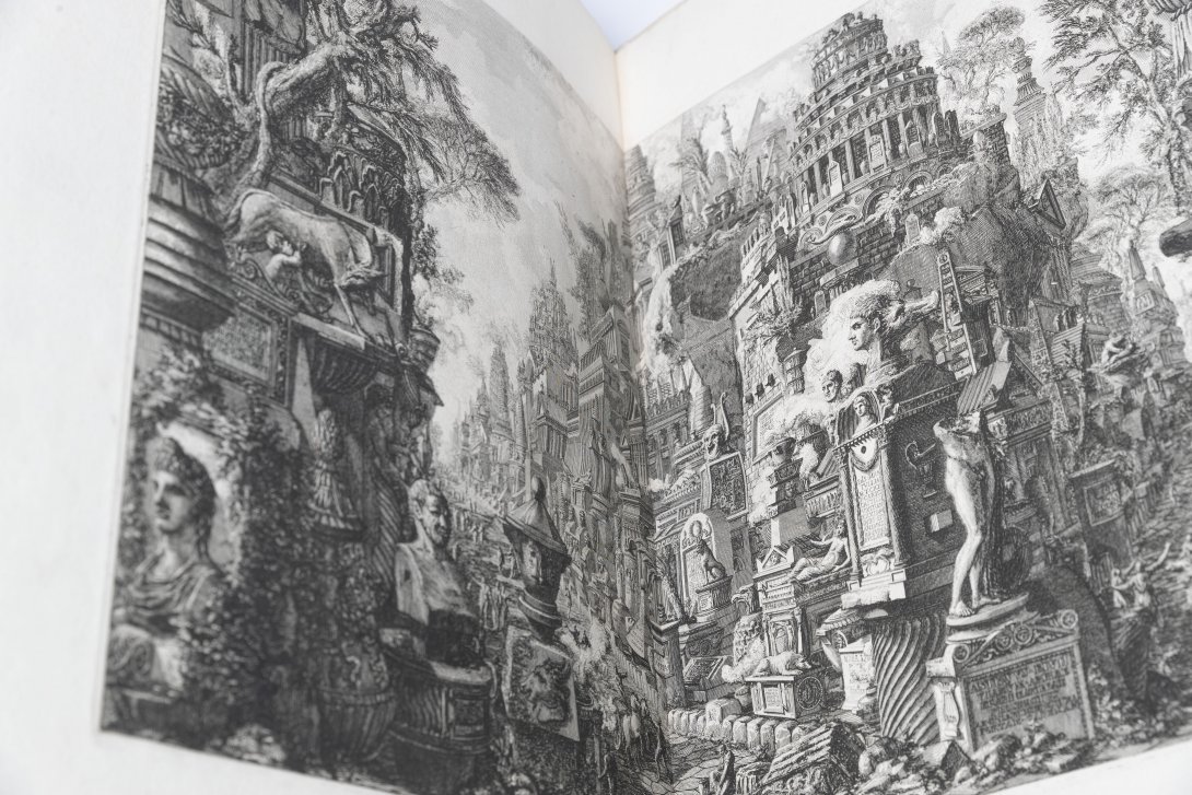 An old book open to show a two page spread of black and white engraved ancient city.