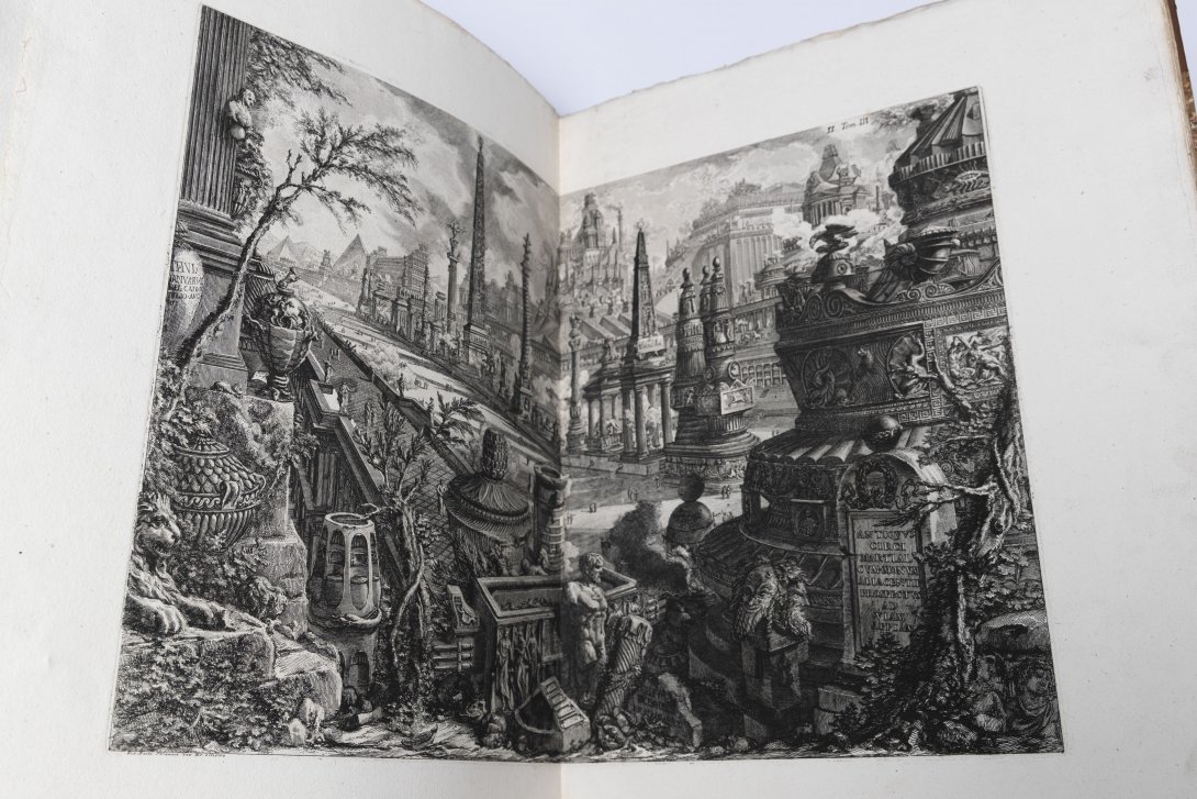 An old book open to show a two page spread of black and white engraved city.